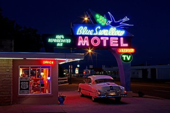 car pulling into classic 70's motel drive in. With neon signs that say "motel"