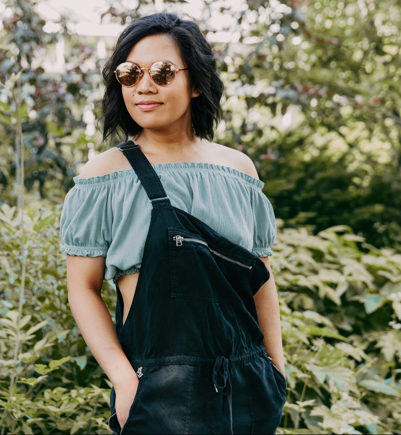 stylish confident woman wearing sunglasses and overalls in front of a field