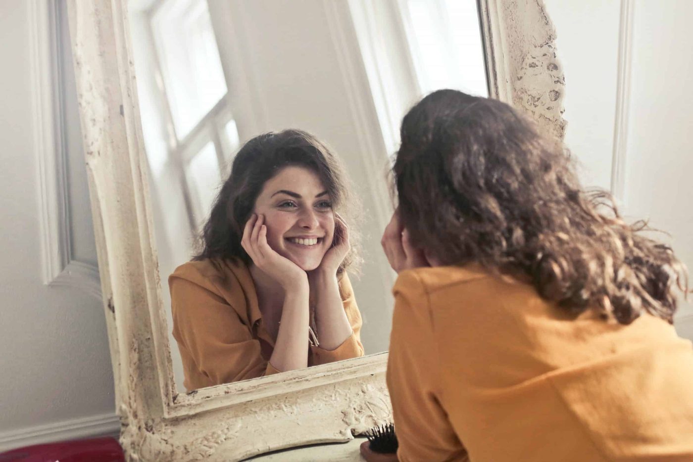 woman cupping her head in both hands looking in the mirror and smiling