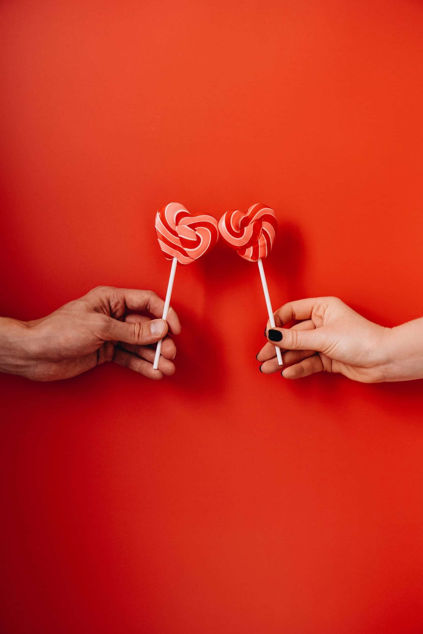 A woman and a man's hands holding heart shaped lolipops in font of red background