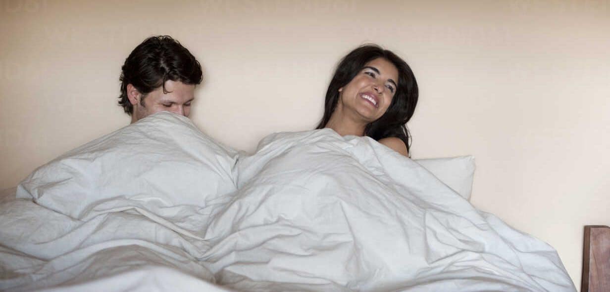 Couple Laughing In Bed Under Blankets