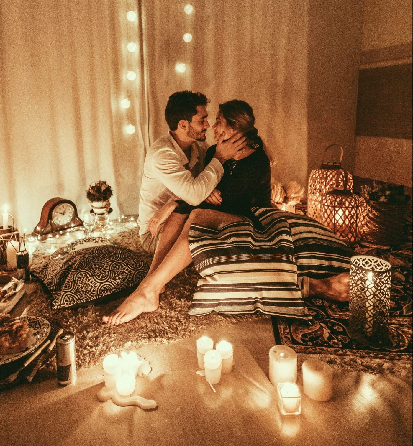 couple sitting close and holding each other in a room with lit candles and a romantic atmosphere