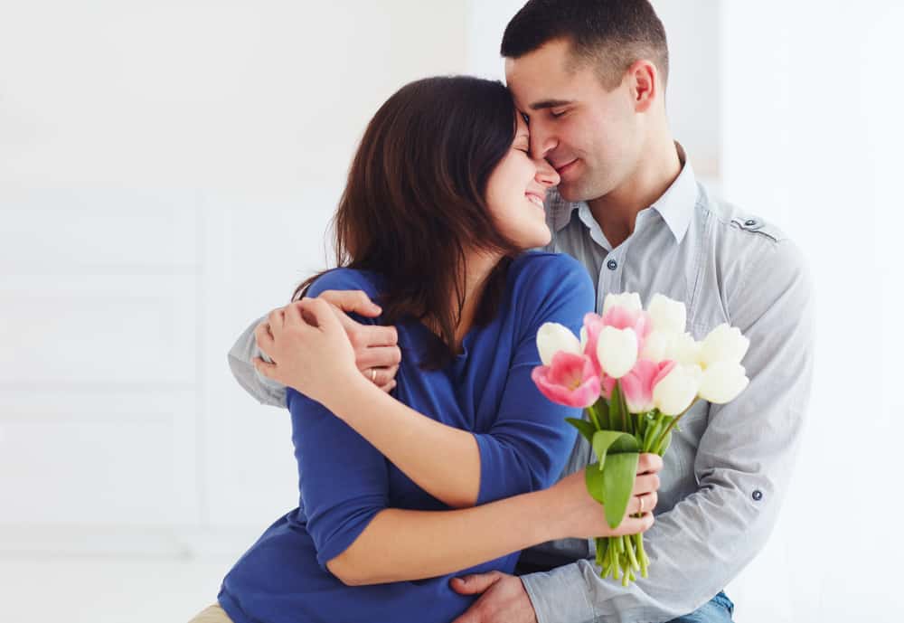 wife hugging husband holding flowers