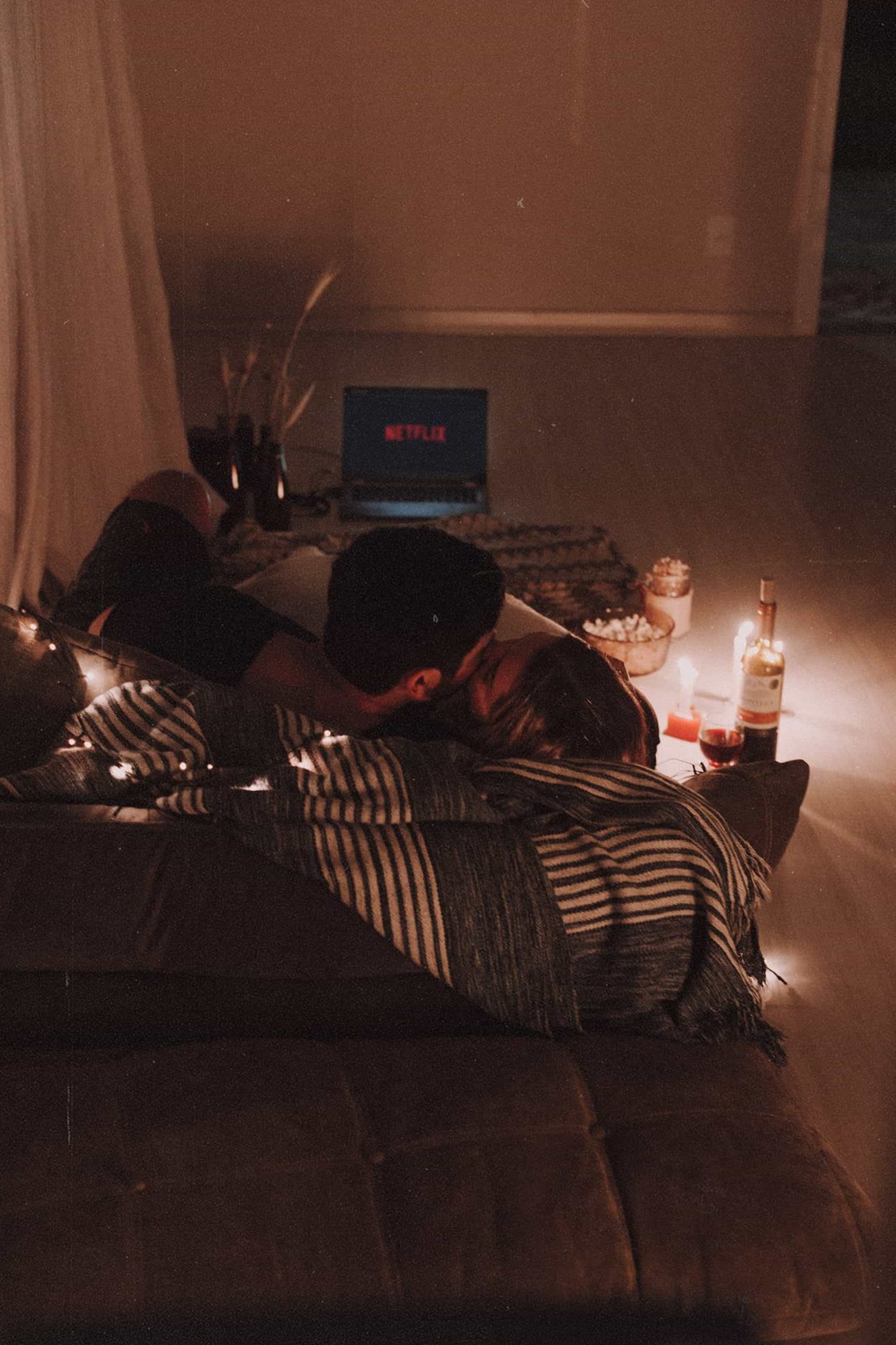 Couple having some netflix and chill, cuddling on the sofa with popcorn, candles and a bottle of wine