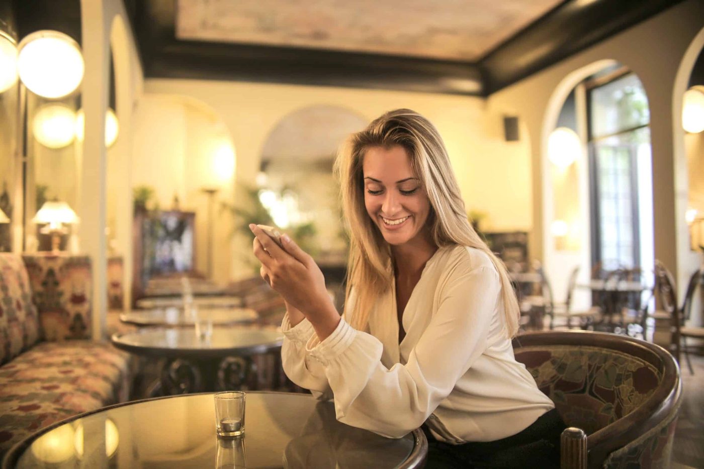 Woman sitting at restaurant with her boyfriend holding her smartphone and smiling
