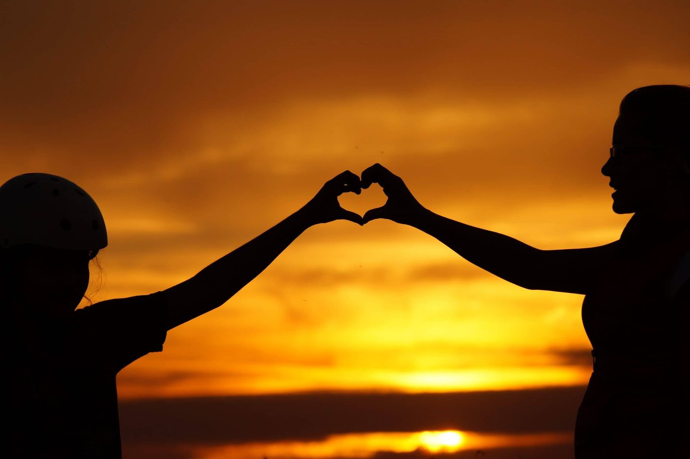 couple on the beach holding arms up and creating joined heart shape at sundown
