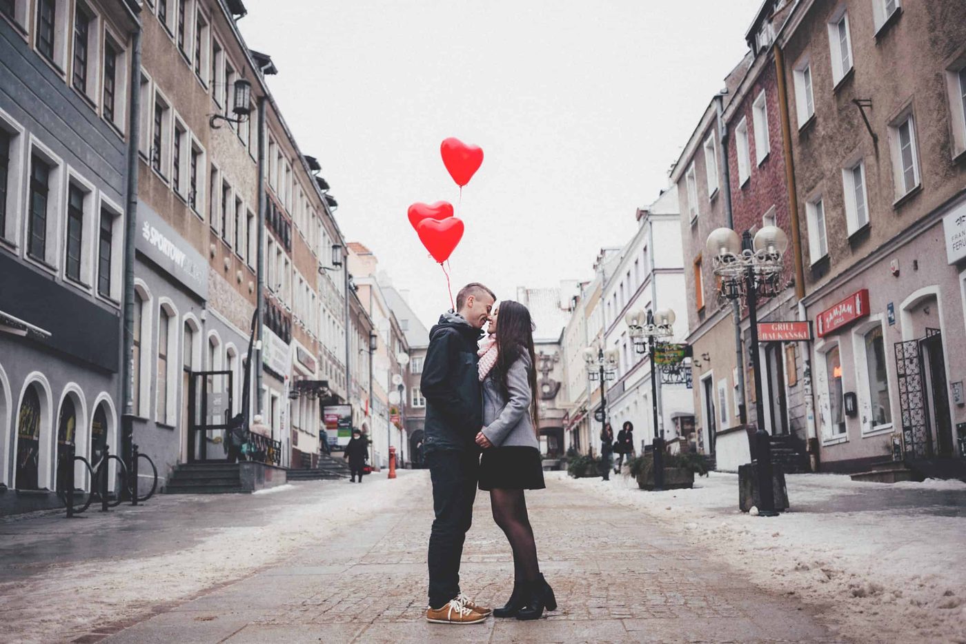 man holding heart shaped baloons kissing his girlfriend in the middle of the street