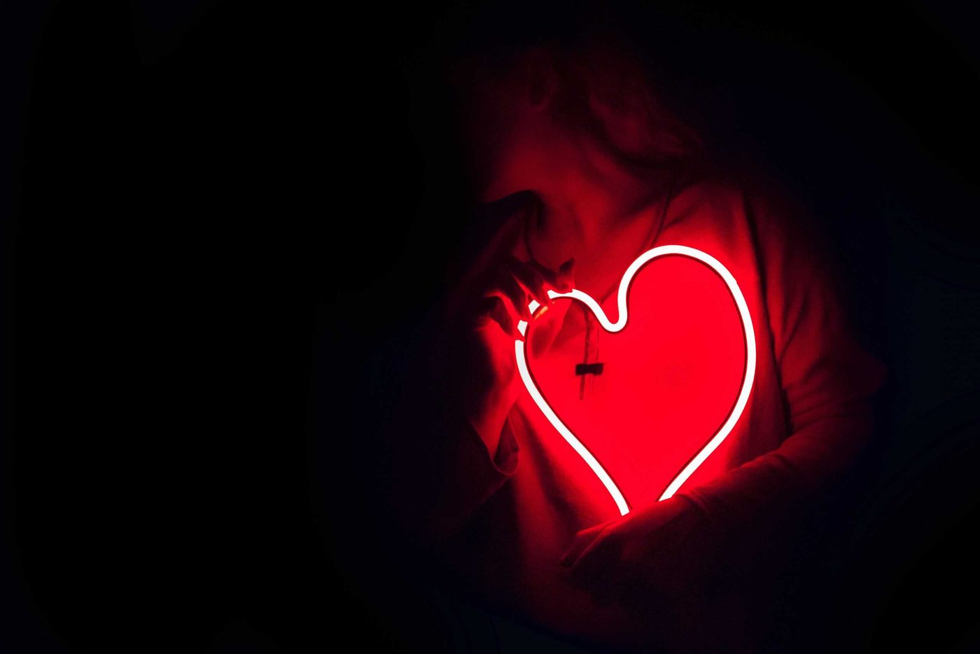 woman holding heart shaped neon sign close to her chest