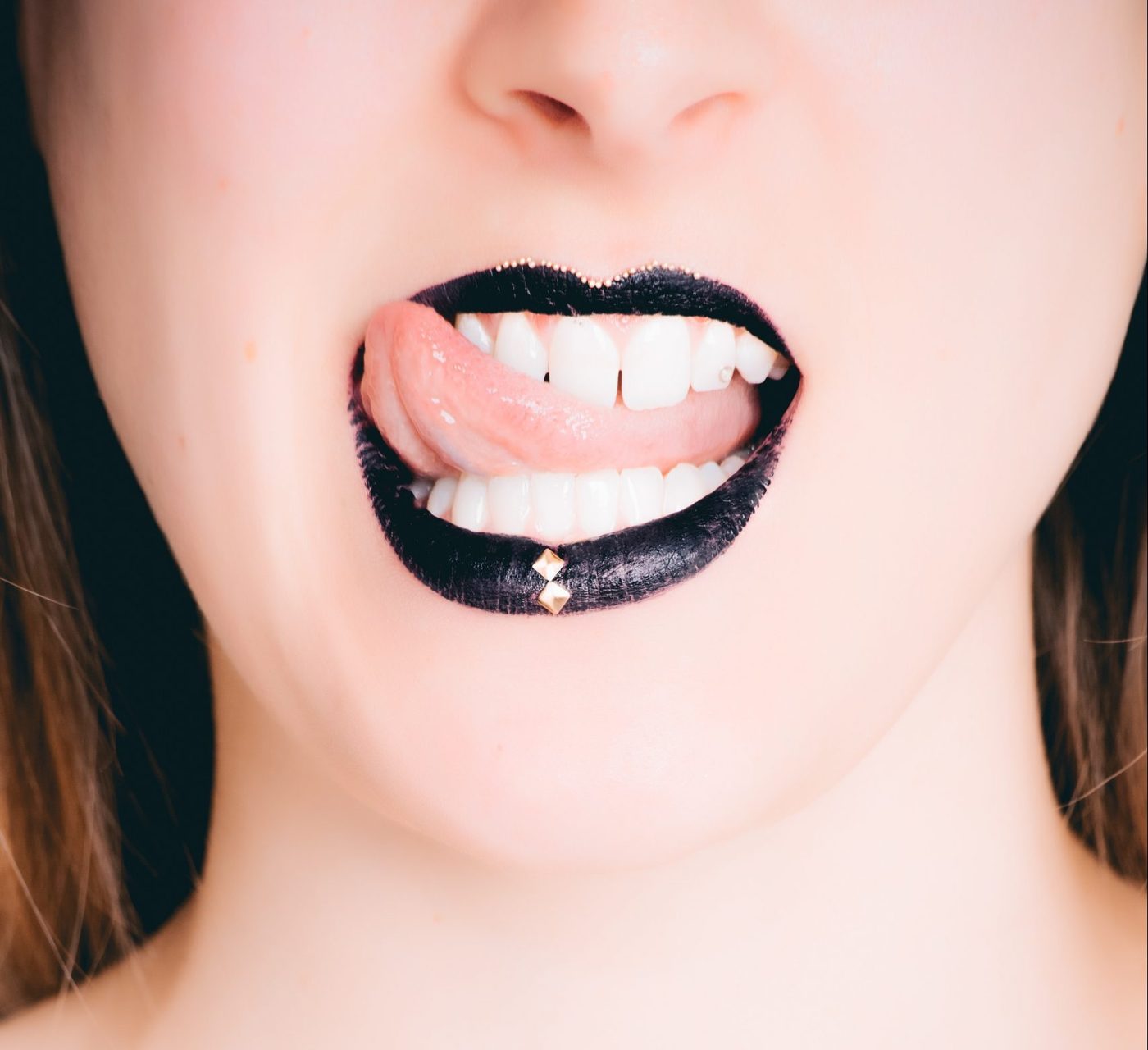 cropped woman's face wearing black lipstick and licking her lips