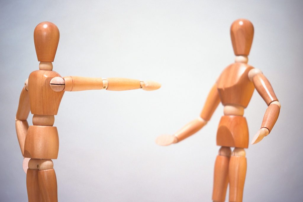 wooden figures, male and female,  one pointing at the other