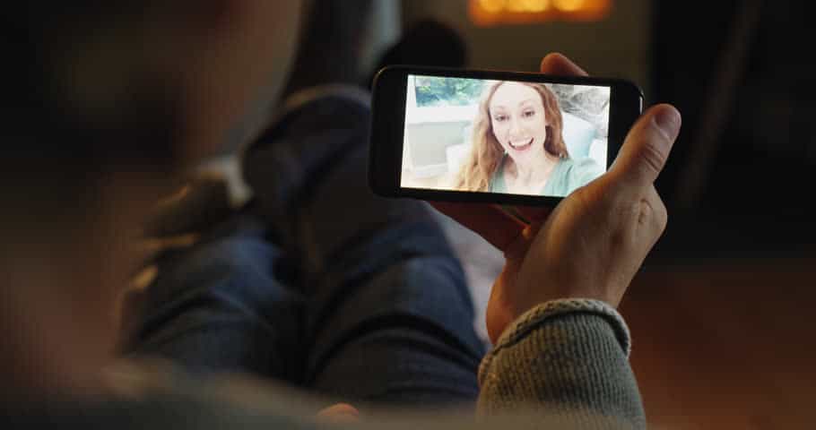 man sitting down holding his smartphone with his female partner on video call