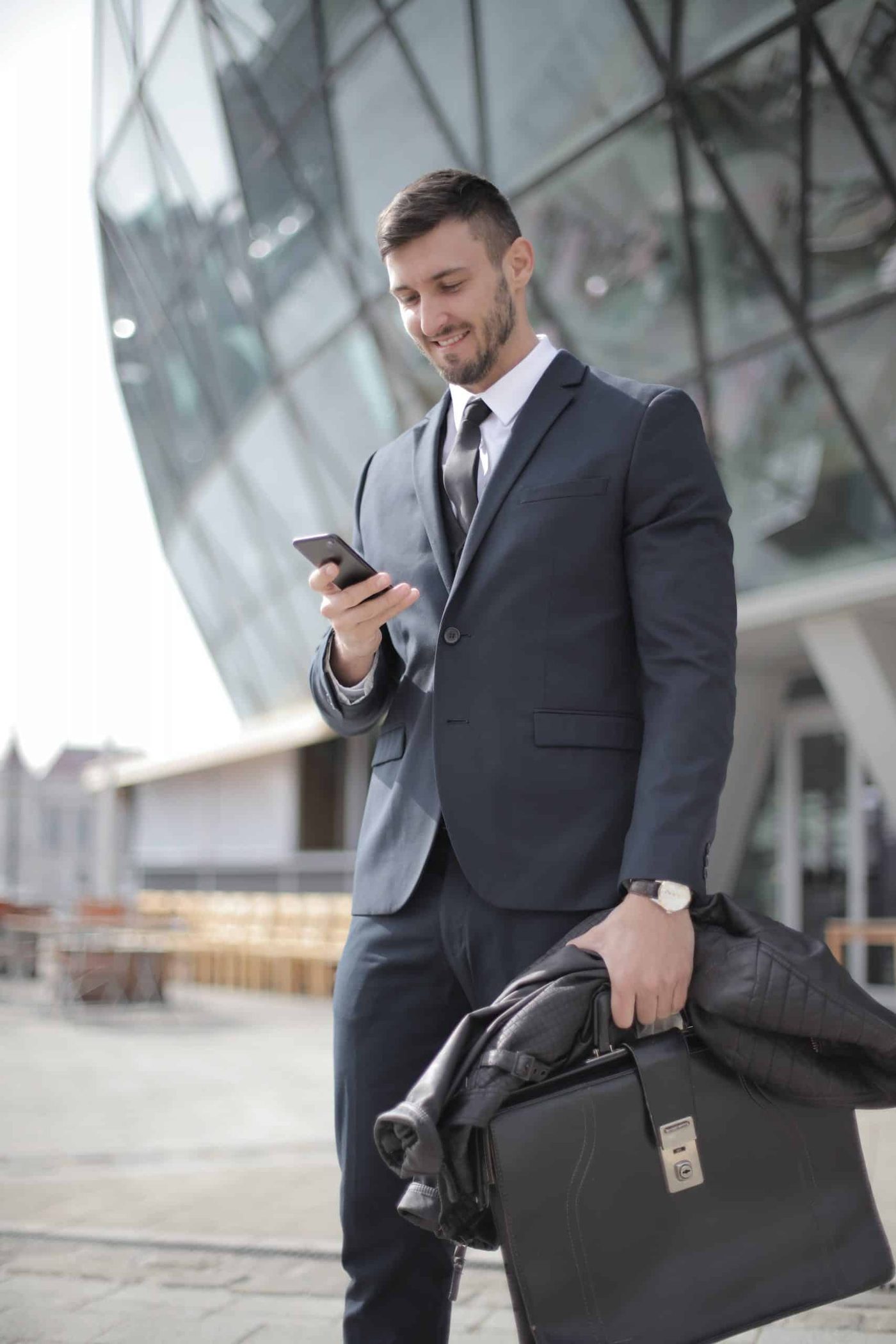 man in suit holding briefcase and looking at his smartphone smiling