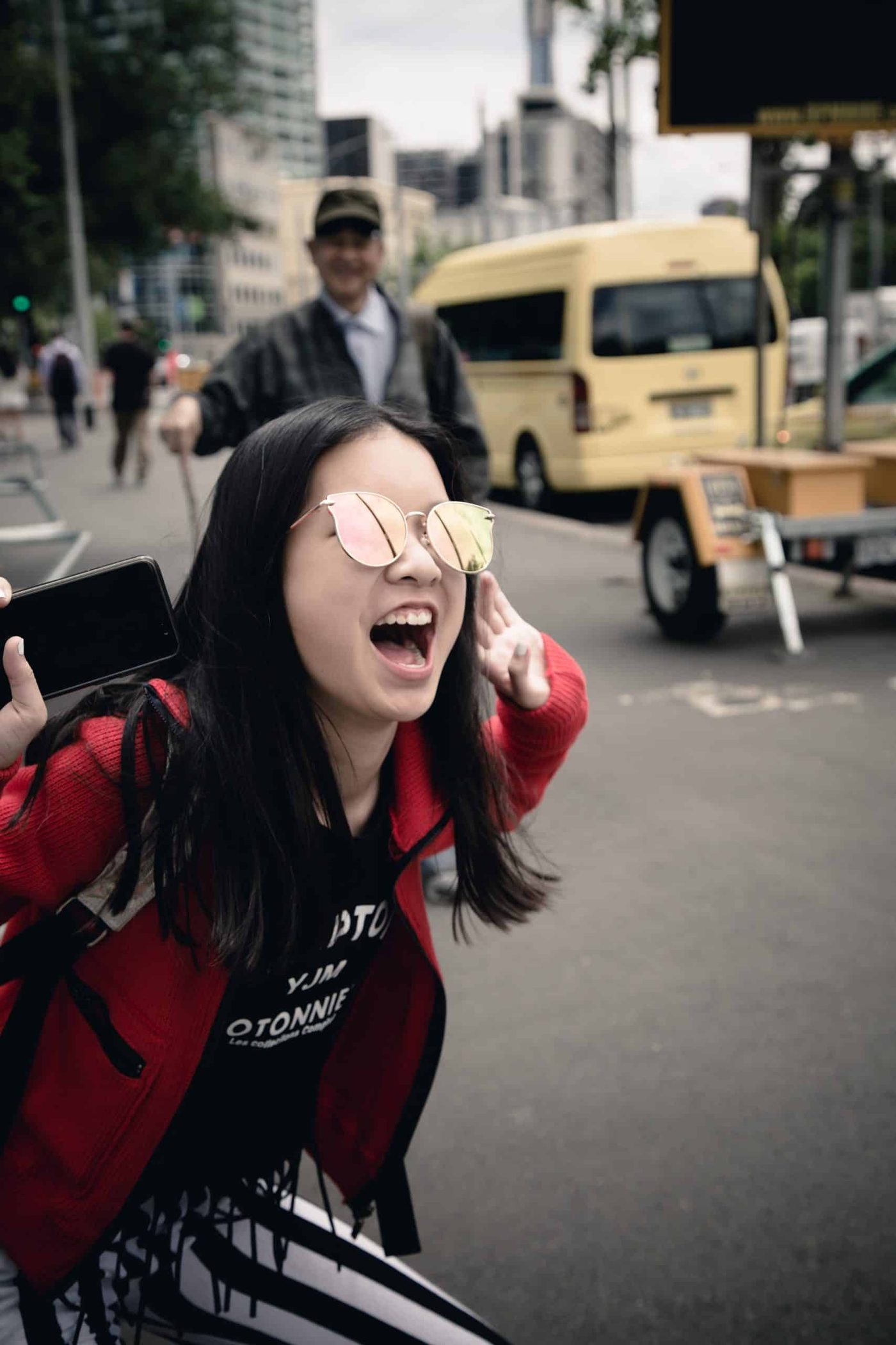 happy woman wearing sunglasses and holding her phone smiling and laughing on streetwalk