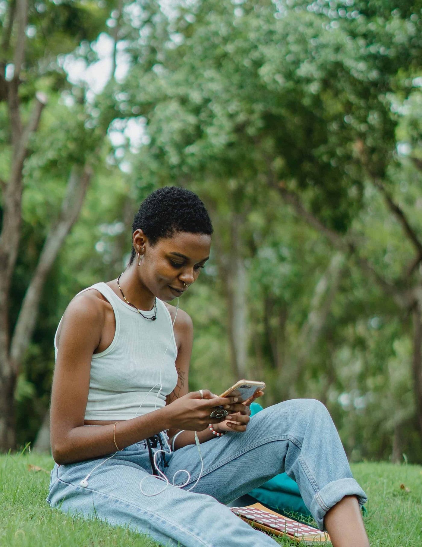 smiling african american woman sitting on the grass using her smartphone