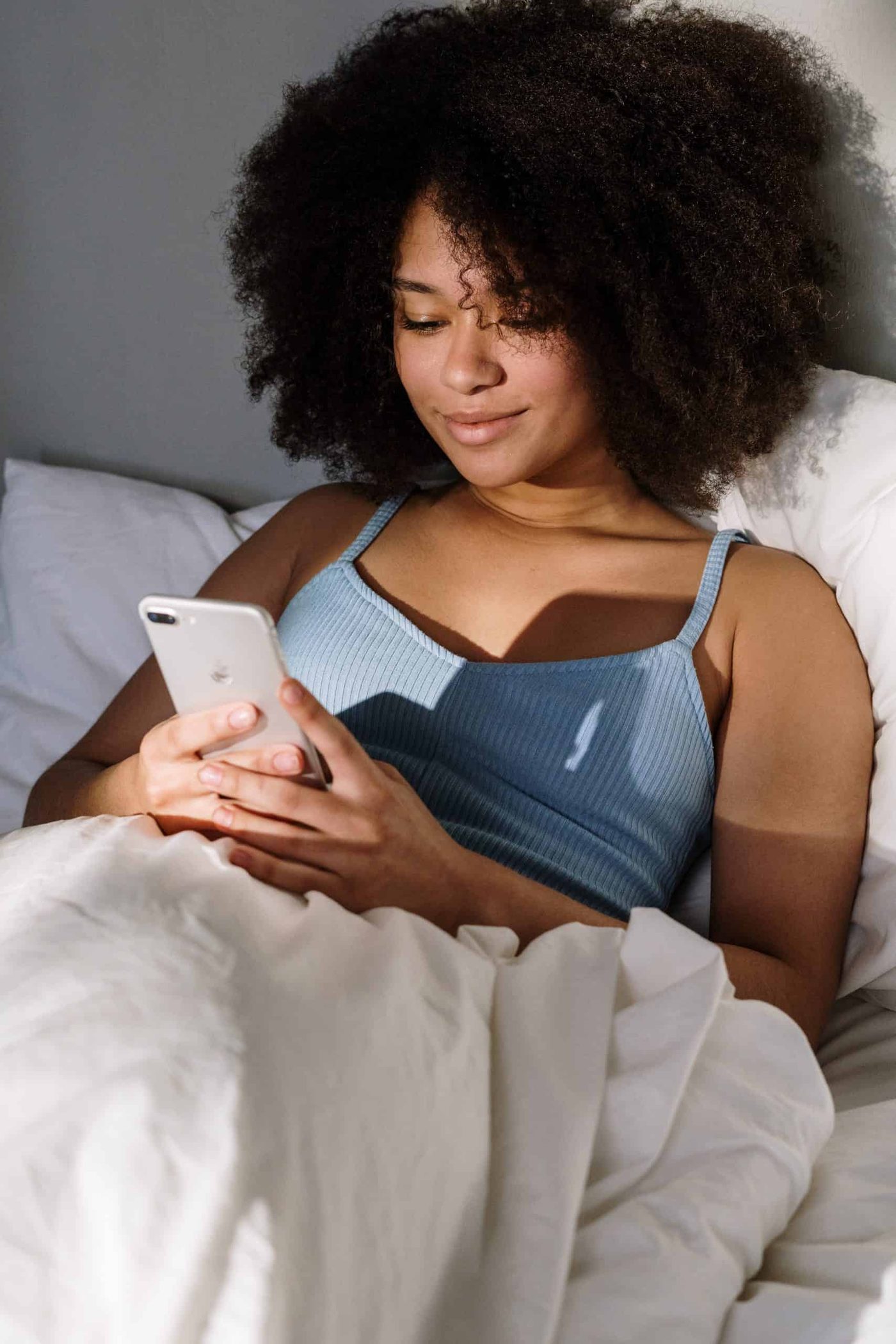 woman lying down in bed smiling and texting on her smarphone