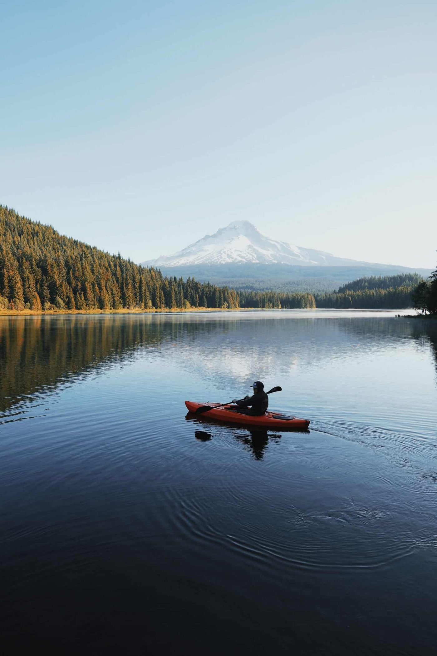 person riding kayak on river in front of mountains and forest in the background