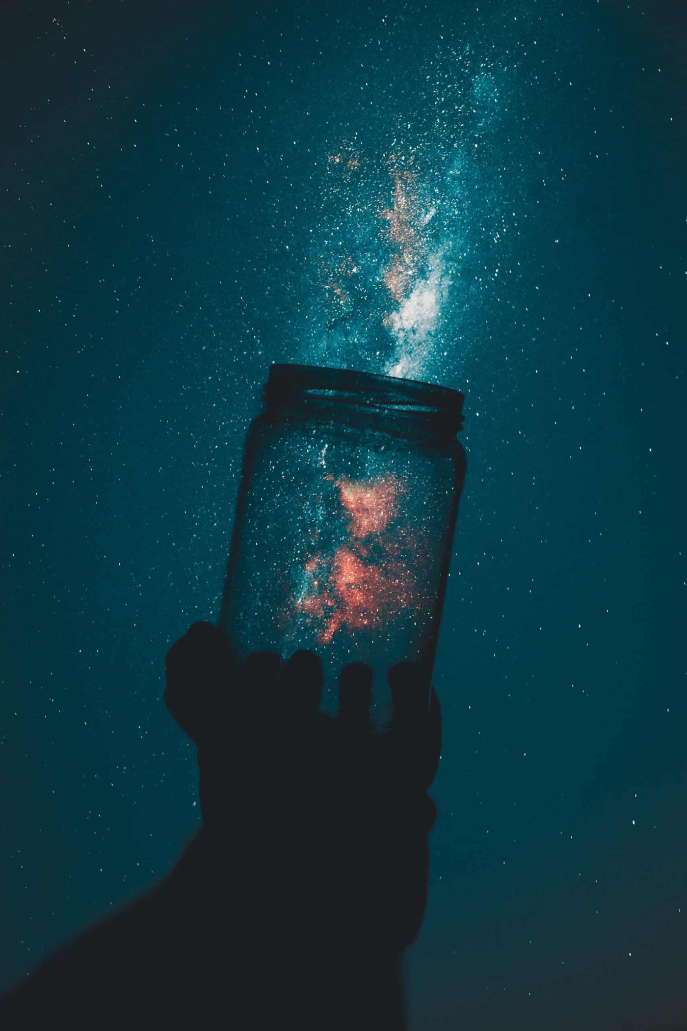 silhouette of hand holding a glass jar pointed at night sky, capturing stars