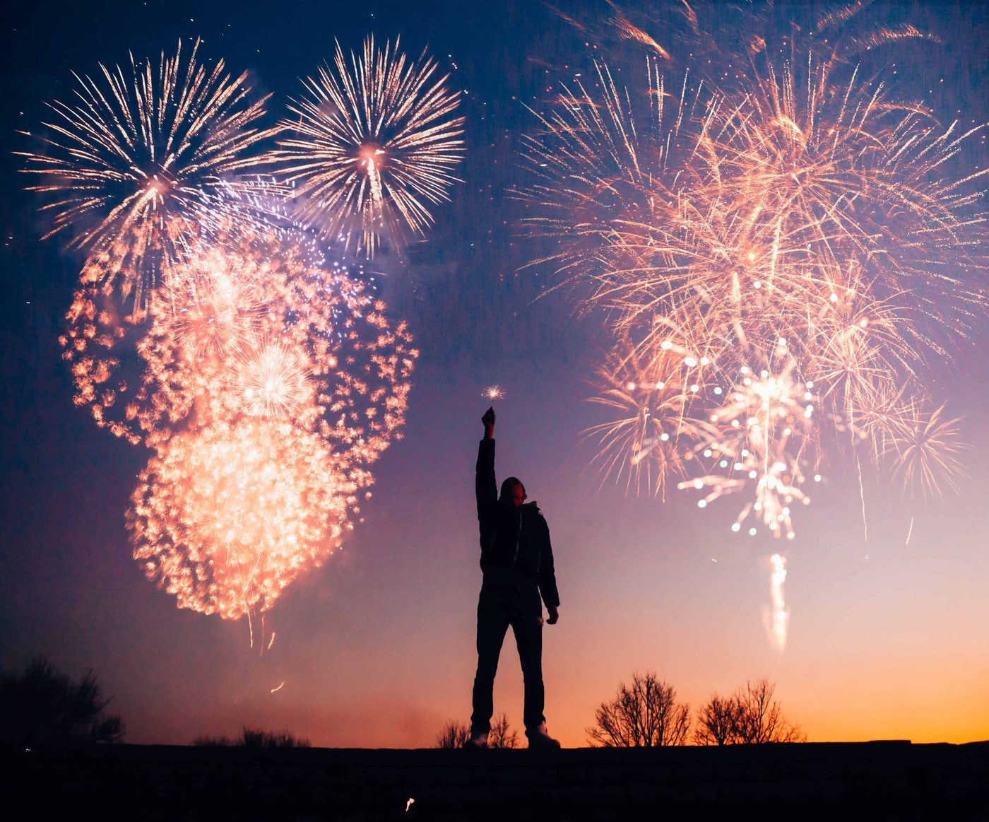 man holding light with far away fireworks during sunset