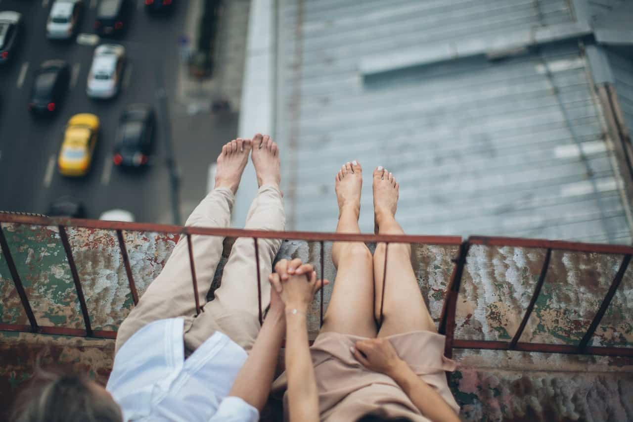 Barefoot man and woman sitting on bridge holding hands with their legs hanging out over a freeway