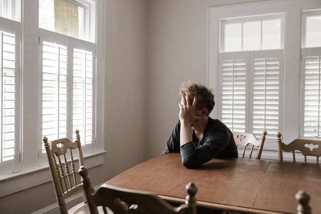 guy in dining room looking stressed and holding is head