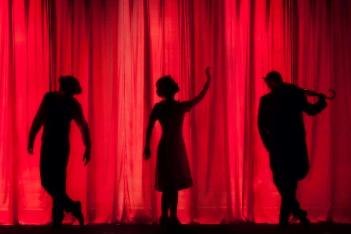 silhouette of musicians and dancers behind a red curtain