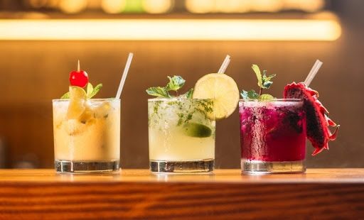 3 beautiful cocktails with straws and herbs on a bar