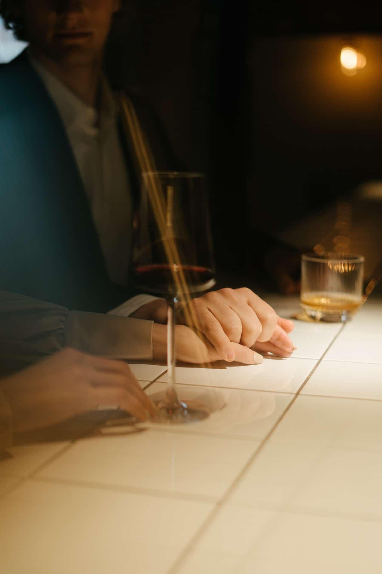 cropped man and woman sitting at the bar gently holding hands and having a drink