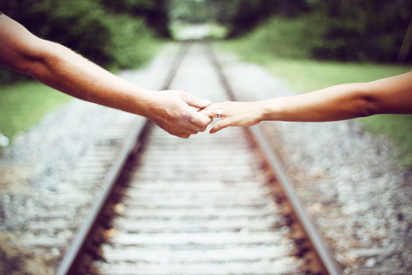 couple holding hands over a railroad leading into a forest
