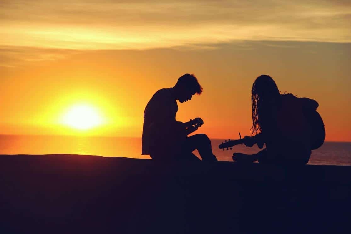 silhouette of couple playing music and having fun during sunset at the beach
