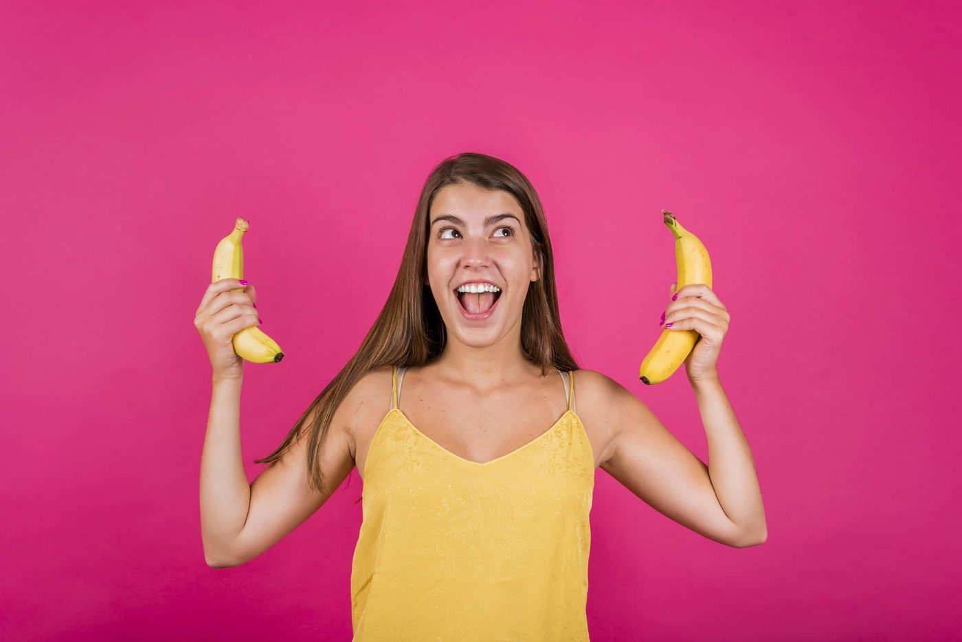 happy young woman with bananas pink background