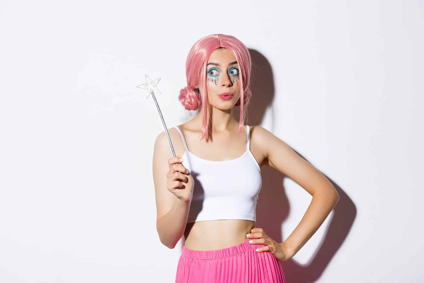 woman with pink wig and bright makeup, holding magic wand, cosplay fairy for halloween party, standing over white background
