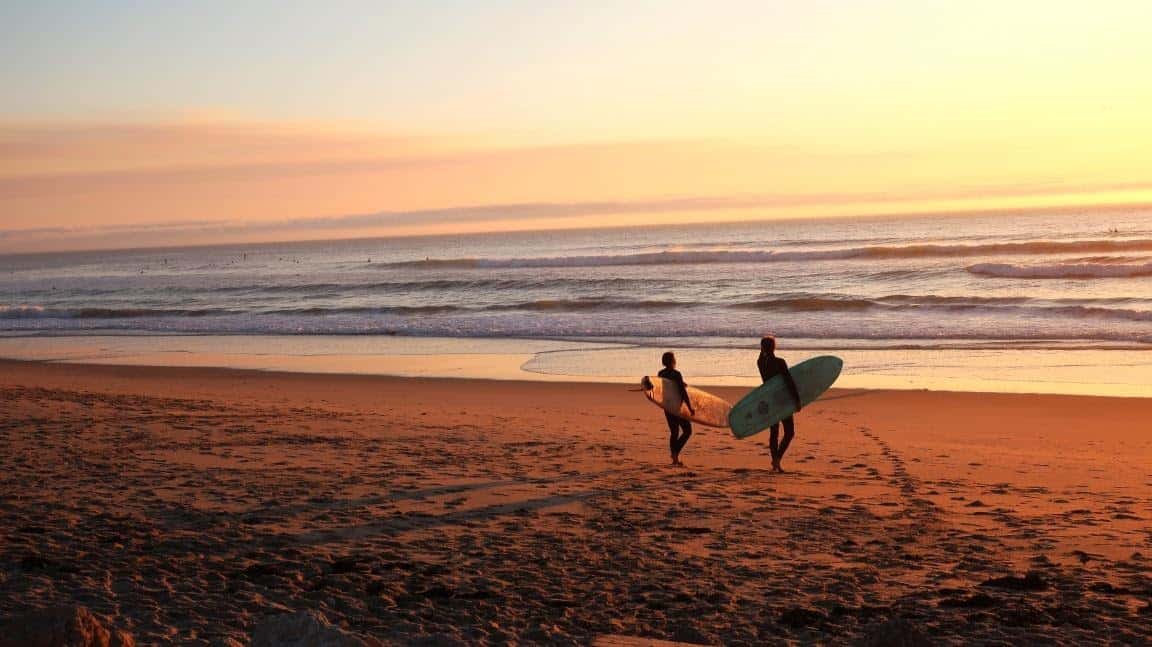 couple walking on the beach at sunset holding surfboards