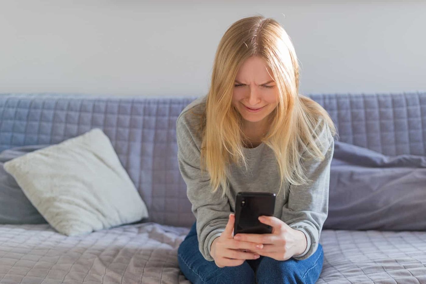 ad blonde woman checking phone sitting sitting on the sofa in the living room at home